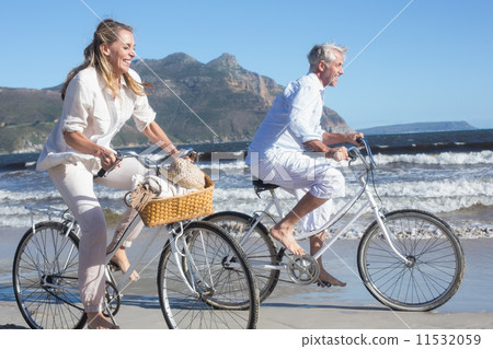 Smiling couple riding their bikes on the beach Smiling couple riding their bikes on the beach 11532059