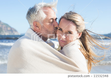 Smiling couple wrapped up in blanket on the beach Smiling couple wrapped up in blanket on the beach 11532348