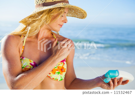 Gorgeous blonde in bikini applying suncream on the beach 11532467