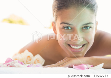 Smiling brunette lying on towel with rose petals 11532714