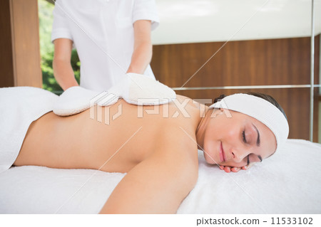 Beauty therapist rubbing womans back with heated mitts Beauty therapist rubbing womans back with heated mitts 11533102