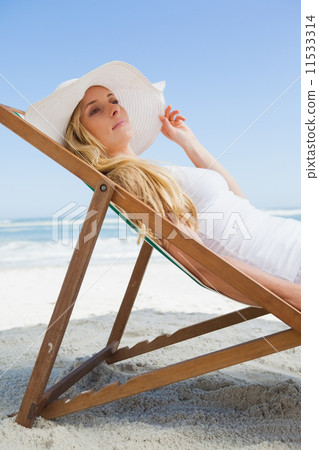 Gorgeous blonde sitting at the beach wearing sunhat 11533314