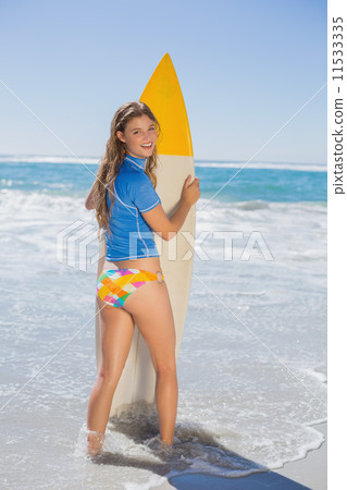 Fit smiling surfer girl standing on the beach with her surfboard Fit smiling surfer girl standing on the beach with her surfboard 11533335