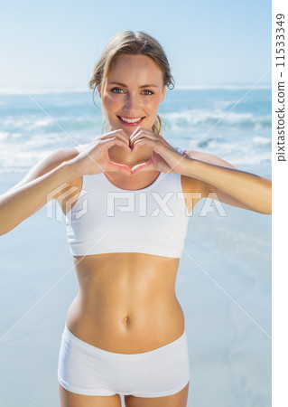 Gorgeous fit blonde making heart shape with hands by the sea Gorgeous fit blonde making heart shape with hands by the sea 11533349