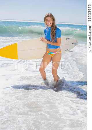 Fit smiling surfer girl on the beach with her surfboard Fit smiling surfer girl on the beach with her surfboard 11533436