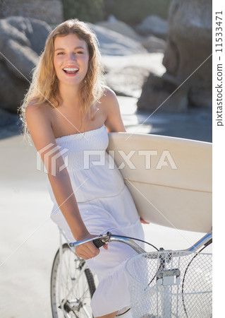 Beautiful surfer in sundress on bike holding surfboard at the be Beautiful surfer in sundress on bike holding surfboard at the be 11533471