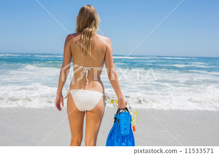 Fit woman in white bikini holding snorkeling gear on the beach 11533571