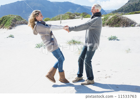 Smiling couple spinning on the beach in warm clothing Smiling couple spinning on the beach in warm clothing 11533763
