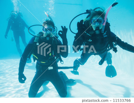 Friends on scuba training submerged in swimming pool two looking 11533766