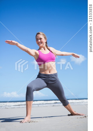 Happy fit blonde standing in warrior position on the beach Happy fit blonde standing in warrior position on the beach 11533858