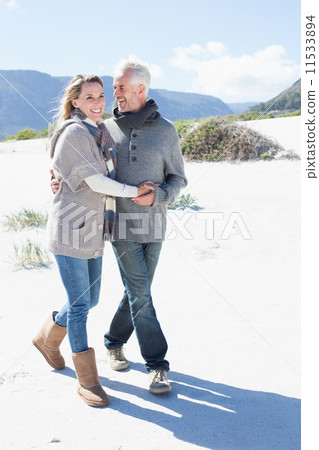 Smiling couple strolling on the beach in warm clothing 11533894