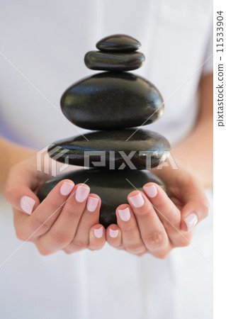 Beauty therapist holding pile of stones for massage Beauty therapist holding pile of stones for massage 11533904