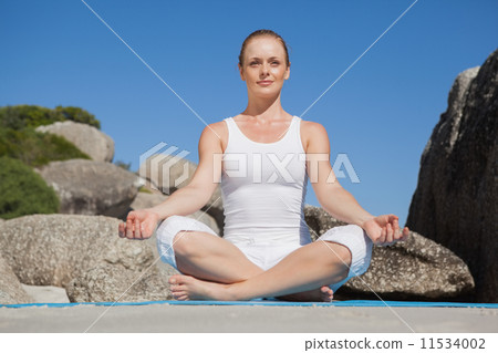 Blonde woman sitting in lotus pose on beach on mat Blonde woman sitting in lotus pose on beach on mat 11534002