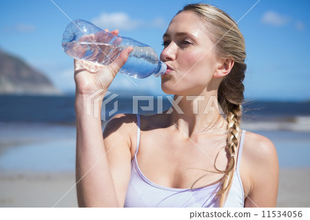 Focused fit blonde drinking water on the beach 11534056