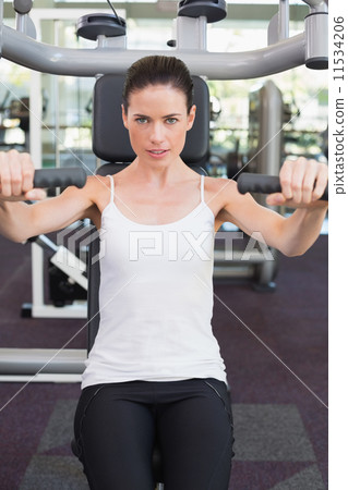Fit brunette smiling at camera using weights machine for arms 11534206
