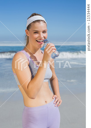 Sporty happy blonde drinking water on the beach 11534444
