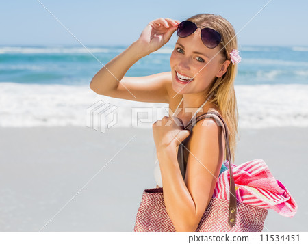 Smiling blonde carrying bag and towel on the beach 11534451