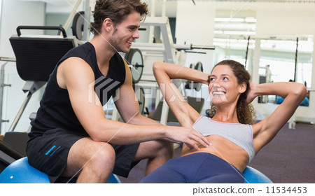 Trainer watching client do sit ups on exercise ball Trainer watching client do sit ups on exercise ball 11534453