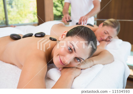 Pretty friends lying on massage tables with hot stones on their 11534593