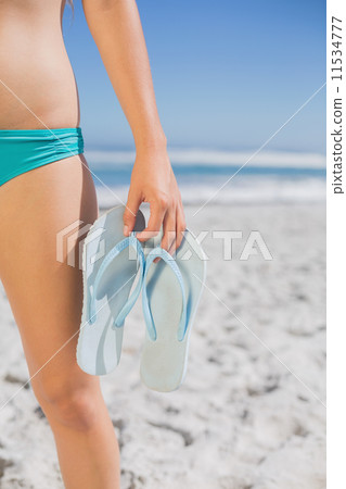 Mid section of fit woman in bikini on beach holding flip flops Mid section of fit woman in bikini on beach holding flip flops 11534777