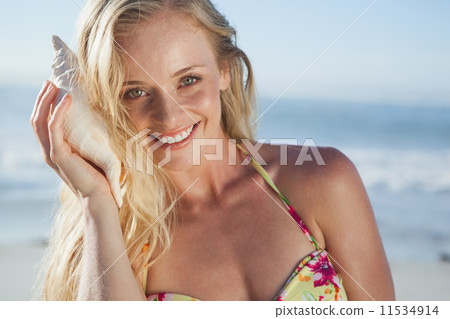 Pretty blonde in bikini listening to conch on the beach Pretty blonde in bikini listening to conch on the beach 11534914