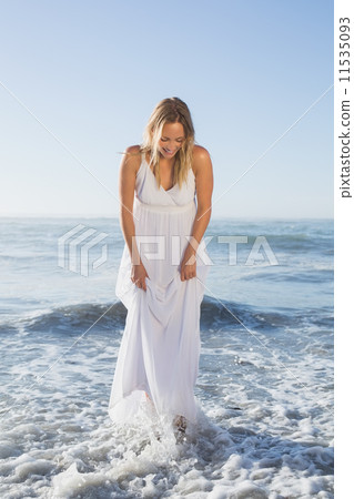 Pretty blonde standing in the sea at the beach in white sundress 11535093