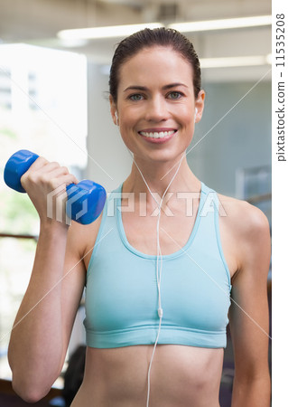Fit brunette lifting blue dumbbell listening to music 11535208