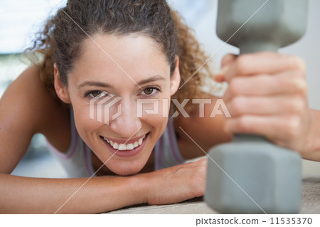 Fit woman smiling at camera holding dumbbell 11535370