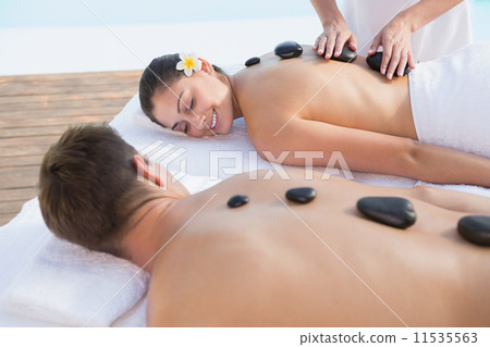 Attractive couple enjoying hot stone massage poolside 11535563