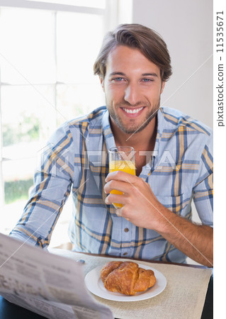 Casual smiling man having orange juice while reading newspaper 11535671