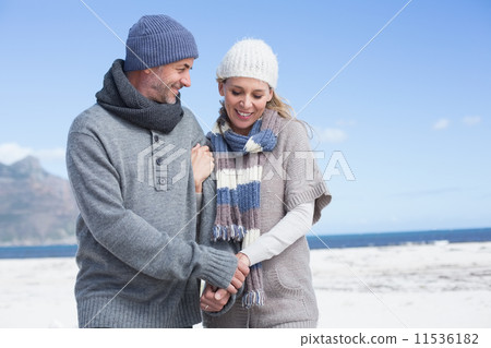Smiling couple standing on the beach in warm clothing Smiling couple standing on the beach in warm clothing 11536182