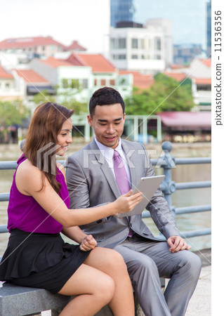 Young Asian business associates having a discussion outdoor using digital tablet  11536356