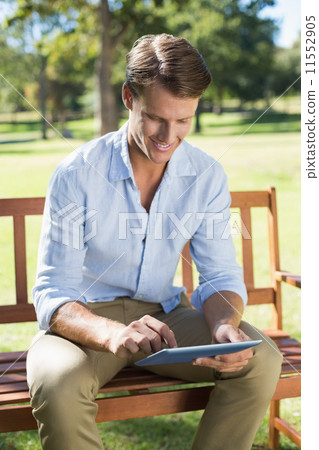 Smiling man sitting on park bench using tablet 11552905