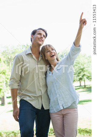 Carefree couple standing in the park with woman pointing 11553413