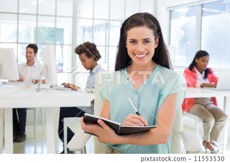 Attractive businesswomen writing in notebook with colleagues beh 11553530