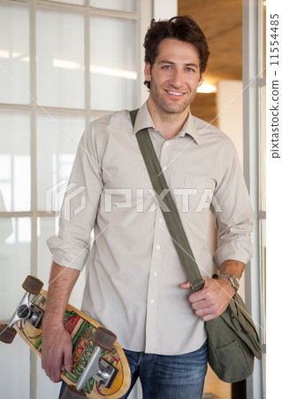 Casual businessman standing with his skateboard smiling at camer 11554485