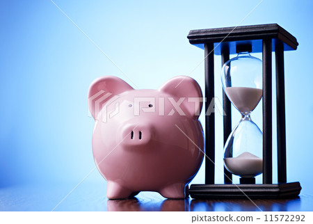 Pink piggy bank with a vintage hourglass behind 11572292