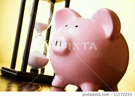 Pink piggy bank with a vintage hourglass behind 11572293