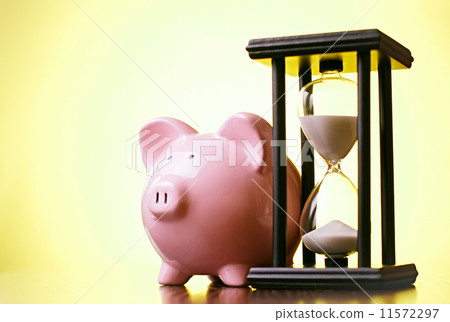 Pink piggy bank with a vintage hourglass behind 11572297