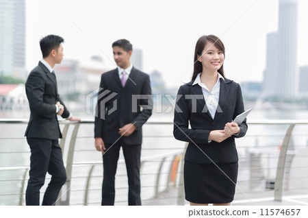 A young dynamic and confident businesswoman posing in the foreground with her colleagues behind A young dynamic and confident businesswoman posing in the foreground with her colleagues behind 11574657