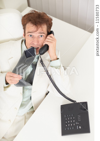 Young businessman speaks on phone, worries and bites tie Young businessman speaks on phone, worries and bites tie 11580733