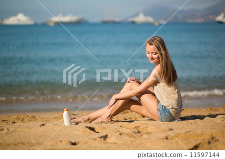 Beautiful woman applying sunscreen on her legs 11597144
