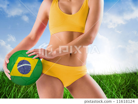 Composite image of fit girl in yellow bikini holding brazil foot 11618124