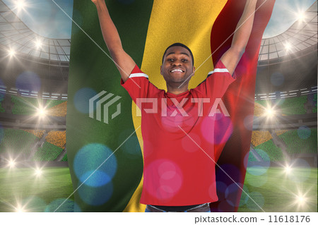 Composite image of excited handsome football fan cheering holdin Composite image of excited handsome football fan cheering holdin 11618176