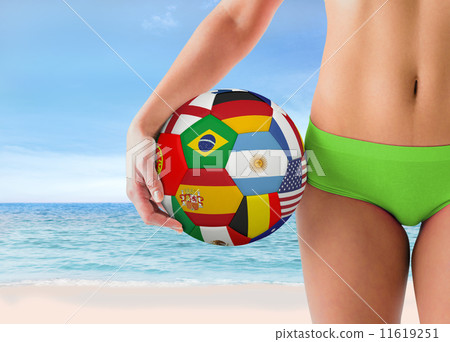 Composite image of fit girl in green bikini holding flag footbal 11619251
