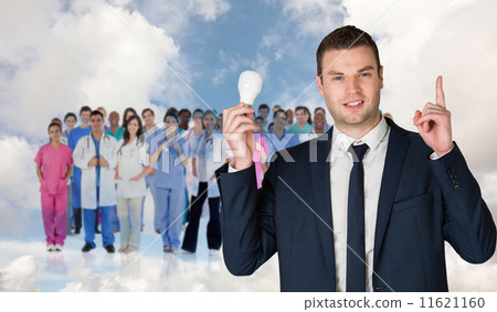 Composite image of businessman holding light bulb and pointing 11621160