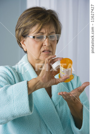 Senior Hispanic woman holding empty medication bottle 11627427