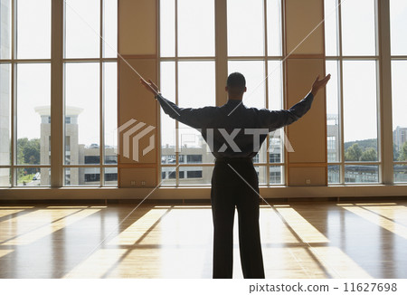 Businessman standing in sunlit room with arms outstretched Businessman standing in sunlit room with arms outstretched 11627698