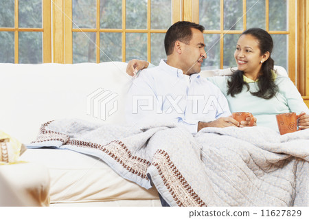 Couple sitting on the couch under a blanket together Couple sitting on the couch under a blanket together 11627829