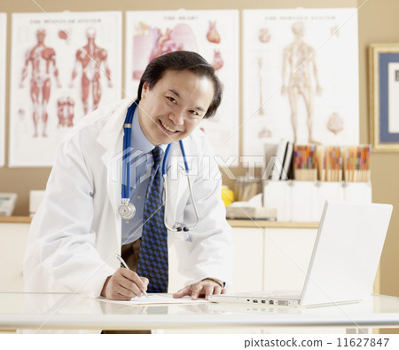 Asian male doctor writing at desk 11627847